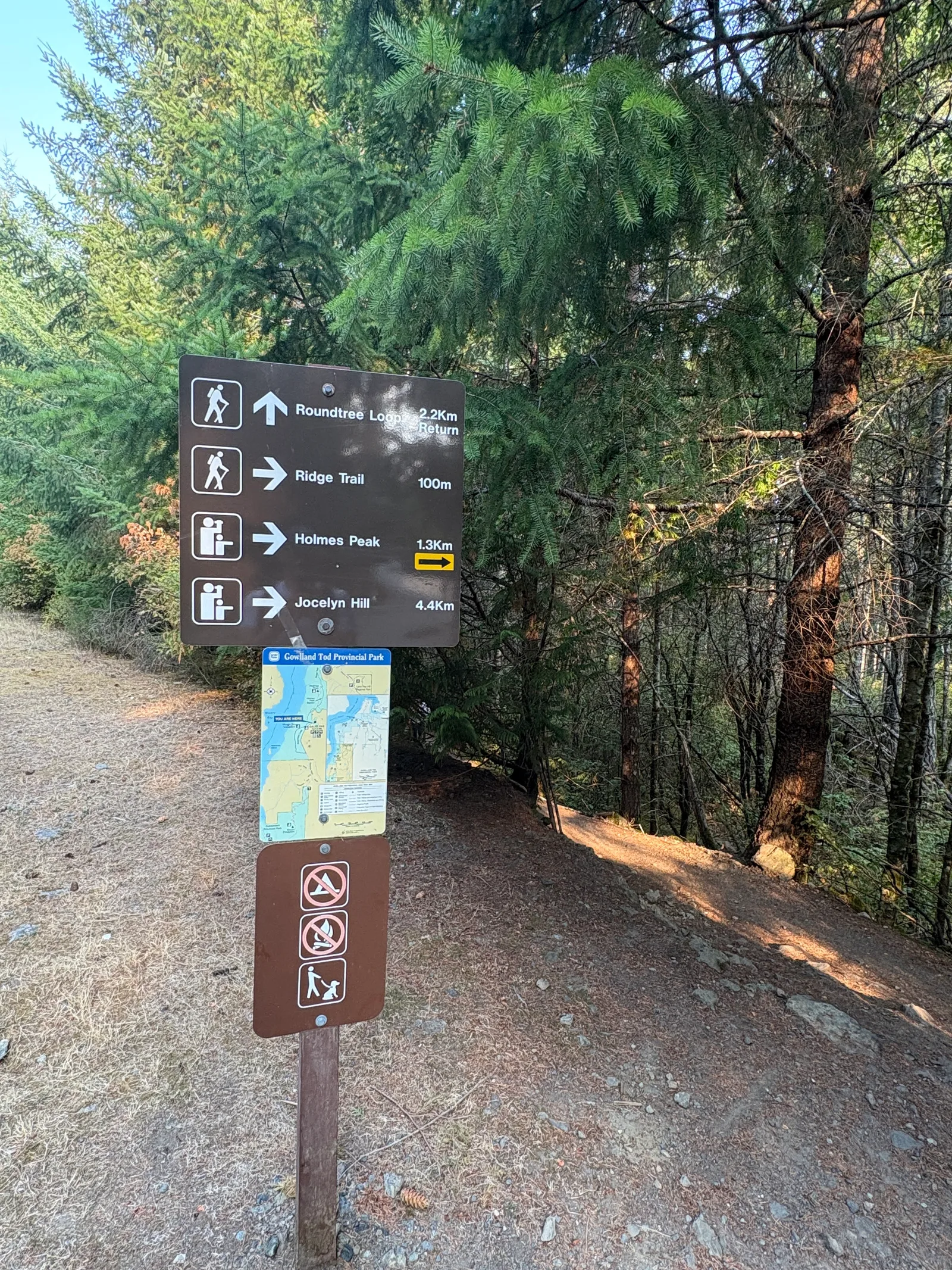 Trail junction signboard in Gowlland Tod Provincial Park showing directional arrows and distances for Jocelyn Hill, Ridge Trail, Holmes Peak, and the Roundtree Loop return