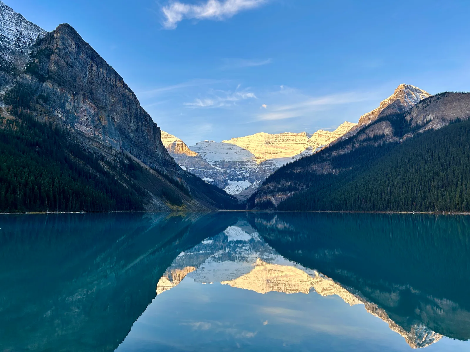 Lake Louise at sunrise with no other visitors on the shore, turquoise water perfectly still, snow-capped peaks and their reflection filling the frame