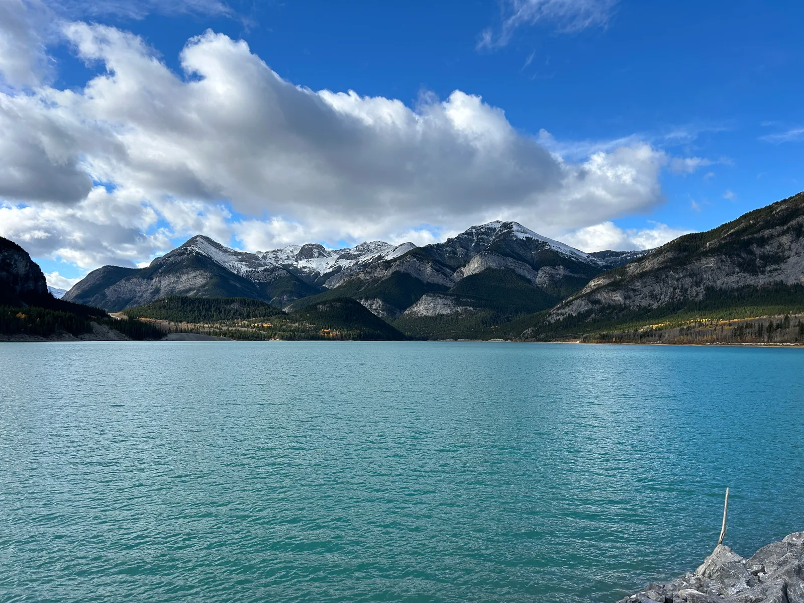 Turquoise Barrier Lake seen from the parking lot at the Prairie View trailhead, snow-dusted mountains rising behind it under a partly cloudy sky